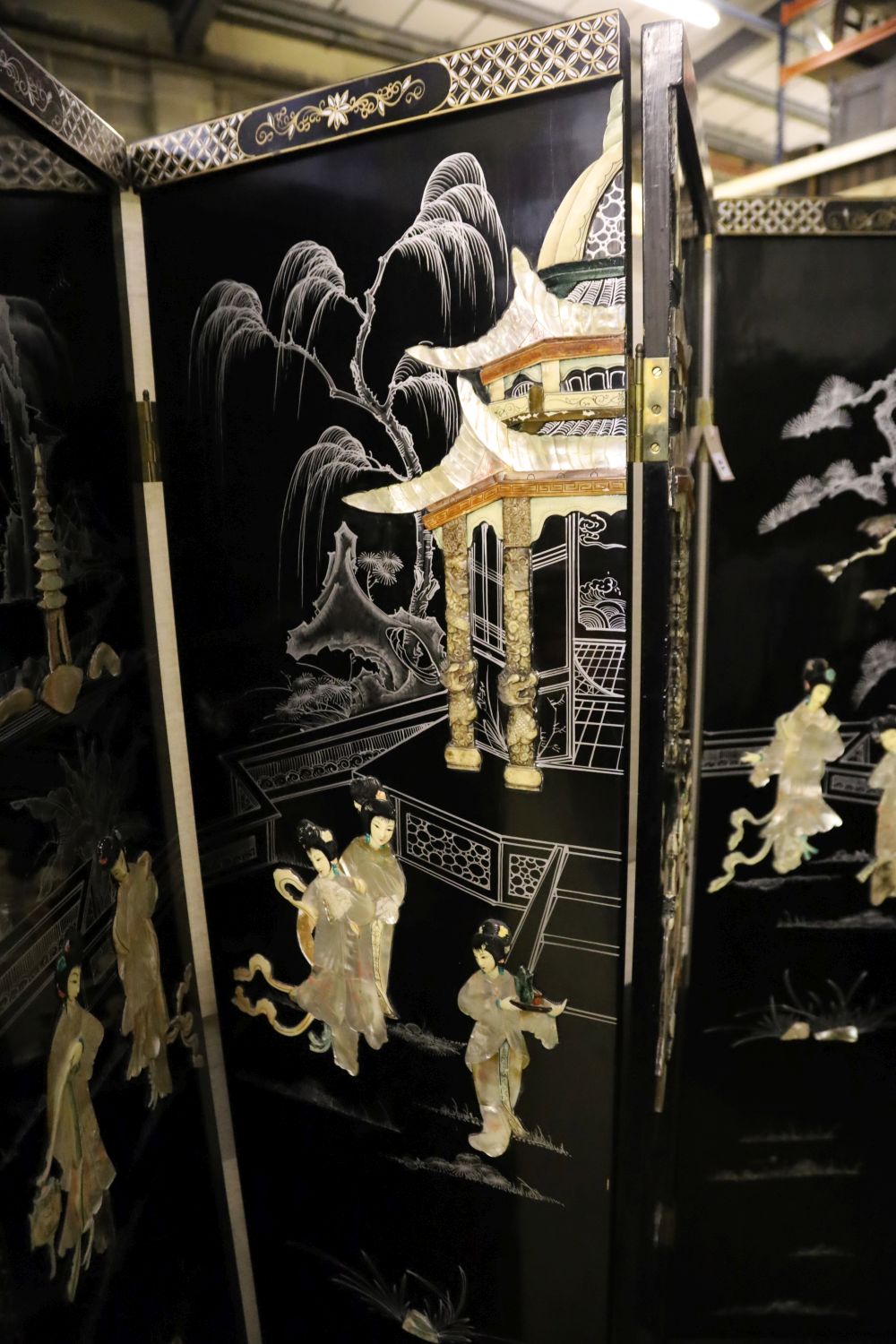 A Japanese black-lacquered and painted four-fold screen with applied decoration of geishas and temple, each panel 46 x 182cm